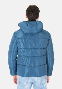 Giacca puffer blu con cappuccio, caratterizzata da sezioni trapuntate e una texture lucida. La parte posteriore mostra una vestibilità comoda e polsini elasticizzati.