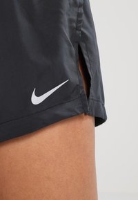 Czarne sportowe szorty wykonane z lekkiego materiału, z białym logo Nike i bocznymi rozcięciami dla zwiększonej swobody ruchu.
