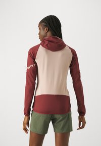 Langärmliger Hoodie in Weinrot und Beige, mit weicher Textur, Kapuze und stilvollem Farbabgleich. Kombiniert mit grünen Shorts.