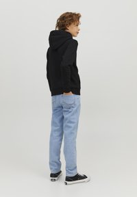 Felpa nera con cappuccio, jeans azzurri e sneakers nere. La felpa ha un design semplice; i jeans hanno un taglio classico.