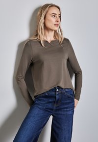 Maglietta a maniche lunghe color verde oliva con un collo a giro delicato, abbinata a jeans a gamba larga blu scuro con vita alta e chiusura a bottoni.