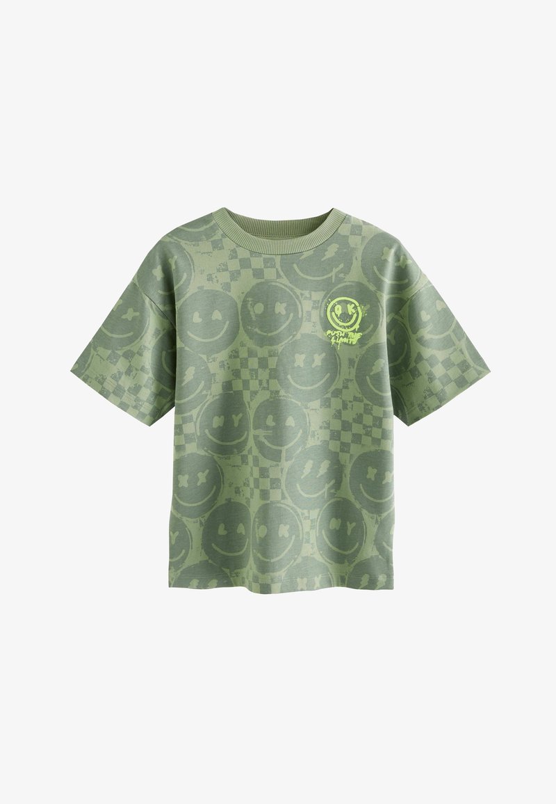 T-shirt verde a maniche corte con volti sorridenti sbiaditi su tutta la superficie e motivo a scacchiera, con un piccolo dettaglio di volto sorridente giallo brillante sul petto.