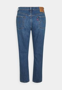 Jeans de mezclilla azul con corte recto, que cuentan con dos bolsillos traseros con un diseño de línea curva y una etiqueta de marca de cuero marrón en la cintura.