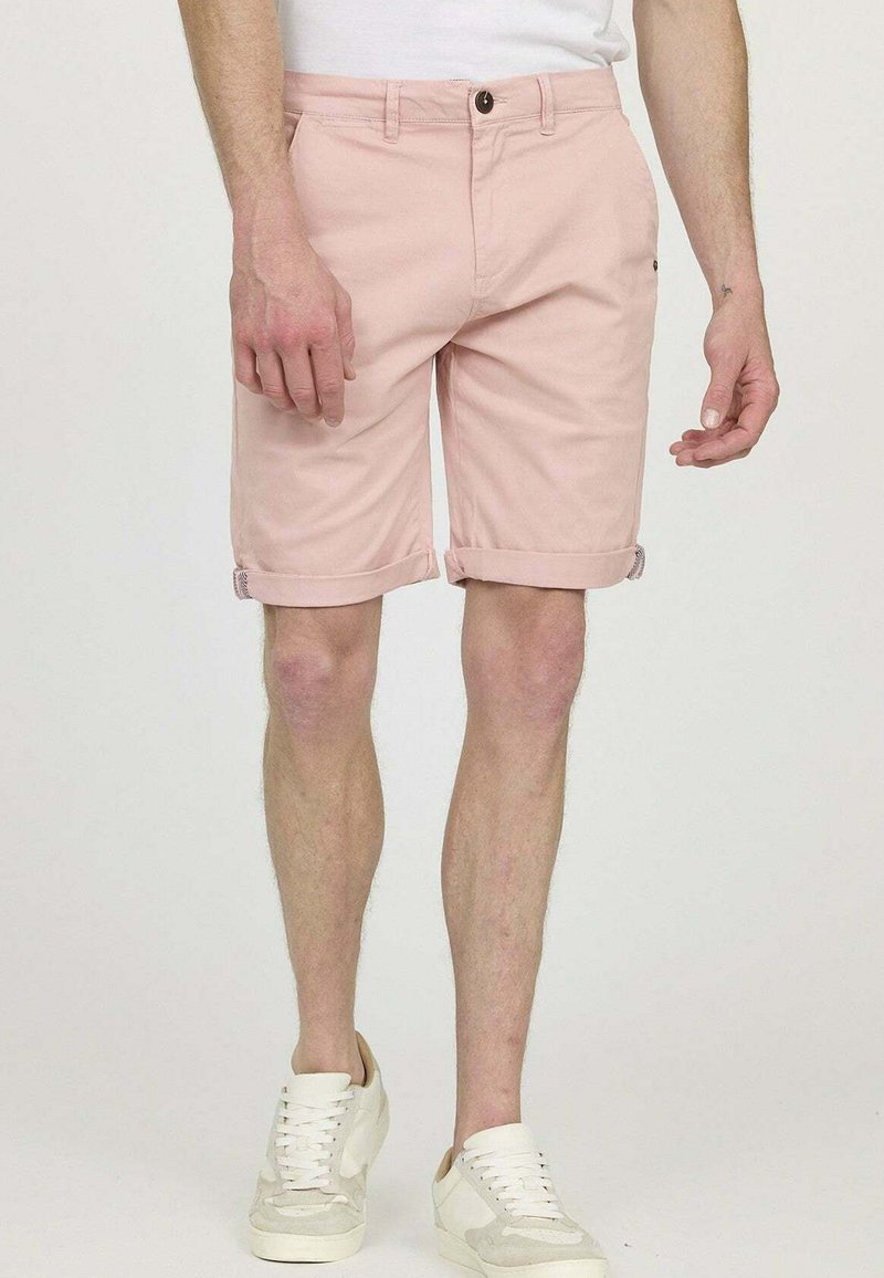 Shorts en coton rose clair avec poches latérales et ourlet roulé. Associés à des baskets blanches, présentant un design décontracté et soigné.