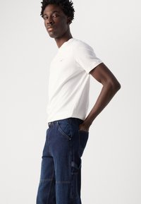 White cotton t-shirt with a round neckline, paired with dark blue denim cargo pants featuring multiple pockets and visible stitching details.