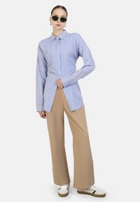Gestreepte lichtblauwe en witte overhemden met lange mouwen, gecombineerd met beige wijdvallende broek en witte sneakers met zwarte accenten.