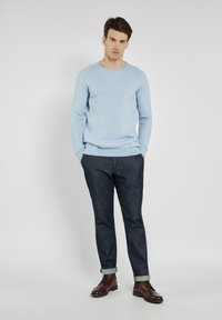 Hellblauer Strickpullover mit rundem Halsauschnitt, getragen mit dunkelblauen Jeans, die am Saum aufgerollt sind, und braunen Lederstiefeln.