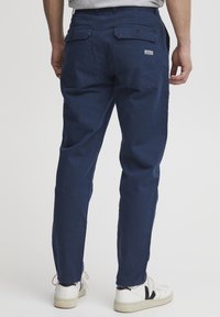 Los pantalones de algodón azul marino cuentan con bolsillos traseros y un diseño de cremallera, complementados con zapatillas blancas con detalles en negro.