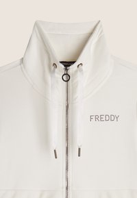 Giacca bianca con zip e colletto alto, dotata di cordini, zip argentata e design "FREDDY" in strass sul lato sinistro del petto.