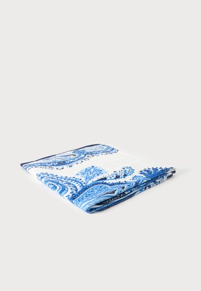 Tissu blanc plié avec des motifs cachemire bleus complexes posé sur un fond clair uni.