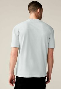 Tricou scurt, de culoare gri deschis, cu o croială lejeră, având guler rotund și detalii subtile de cusătură pe spate.