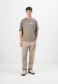 Gray cotton t-shirt with short sleeves, featuring blue and white graphics. Paired with beige cargo pants and white sneakers with brown accents.