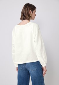 Hvid linned langærmet top med rund halsudskæring og raglanærmer, parret med højtaljede blå denimjeans. Ensfarvet tekstur.