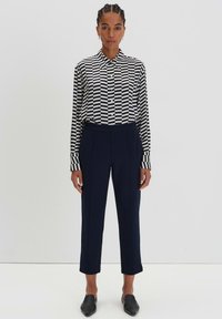 Camicia a righe bianche e nere con bottoni e maniche lunghe, abbinata a pantaloni attillati blu navy e scarpe nere senza lacci. Tessuto dalla texture liscia.