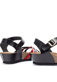 Sandali wedge in pelle nera con plantare in sughero, cinturini incrociati e un accentuazione rossa. Chiusura con fibbia regolabile. Suola in gomma testurizzata.