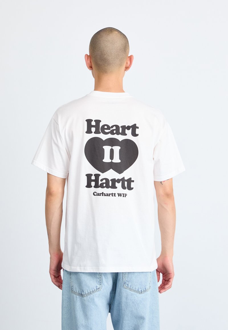 White cotton t-shirt featuring a black graphic design on the back, with text "Heart II Hartt" and "Carhartt WIP" inside a heart shape.