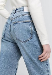 Jeans azzurri a vita alta con un lavaggio sbiadito, caratterizzati da un design a cinque tasche e cuciture visibili. Il tessuto sembra morbido ma resistente.