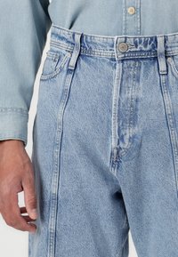 Jeans din denim de un albastru deschis, cu talie înaltă, având un design cu cinci buzunare, cusături vizibile și închidere cu un buton metalic.