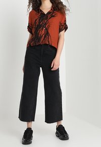 Rostorange kortärmad skjorta med svart abstrakt mönster, tillsammans med högmidjade svarta vida byxor och svarta sneakers.