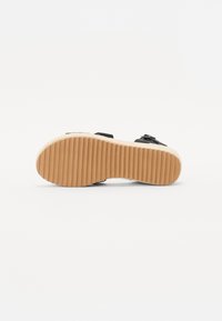 Sandal preta com duas tiras e detalhes de fivela. Sola texturizada e estriada em castanho claro. Palmilha macia e plana para conforto.