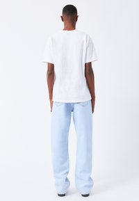 Afslappet hvid bomulds t-shirt med korte ærmer, parret med lyseblå højtaljede jeans, synlige søm og sidelommer.