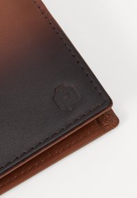Cartera de cuero con una combinación de colores marrón oscuro y marrón claro, textura suave, bordes cosidos y un sutil detalle de logo en relieve.