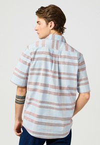 Camicia a maniche corte in cotone azzurro chiaro con strisce orizzontali rosse e marroni; presenta un colletto e un orlo curvato.