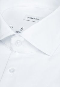 Chemise blanche à col évasé, boutons visibles et étiquette de la marque "seidensticker" à l'intérieur du col.