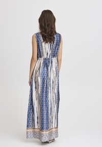 Robe maxi avec un motif bleu et blanc, comprenant des rayures verticales et des accents géométriques, fabriquée en tissu léger avec une taille cintrée.