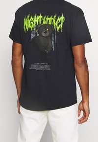 Black cotton T-shirt featuring a green graphic of a bear on the back, with text elements below. Crew neck, short sleeves, relaxed fit.