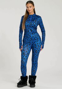Set atletico blu composto da un top a maniche lunghe e leggings con un motivo a stampa leopardata nera. Il top presenta un design con zip a quarto. Stivali neri con bordo in pelliccia.