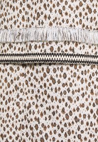 Tekstiili, jossa on bež tausta ja prindi, millel on pruunid ja mustad leopardimustrid. Sisaldab kootud frantsi ja dekoratiivset musta äärist.