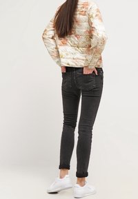 Prošívaná bunda v světle krémové barvě s květinovými vzory v oranžové a zlaté; černé přiléhavé džíny s ohrnutými lemy; bílé tenisky.