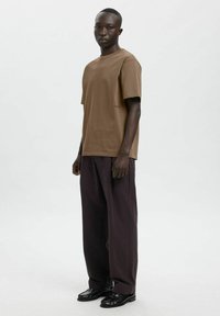 Pruun lühikeste varrukatega puuvillane t-särk, millel on tumelilla laia lõikega püksid ja mustad jalatsid, lihtsa, modernse disainiga.