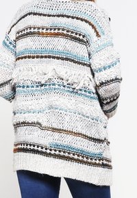 Stickad cardigan med en lös passform, flerfärgade ränder i blått, brunt och krämfärgat, med fransdetaljer i fållen.