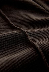 Brązowa ribbed tkanina o miękkiej fakturze, z pionowymi paskami i delikatnymi fałdami, tworzącymi różnorodne wzory światła i cienia.