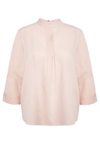 Blouse rose pâle avec un col montant, des manches trois-quarts et de subtils plis à l'avant. Texture lisse, coupe droite et ourlet arrondi.