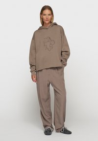 Bruine hooded sweatshirt met een losse pasvorm en grafische tekstontwerp, gecombineerd met wijde bijpassende broeken en donkere schoenen.