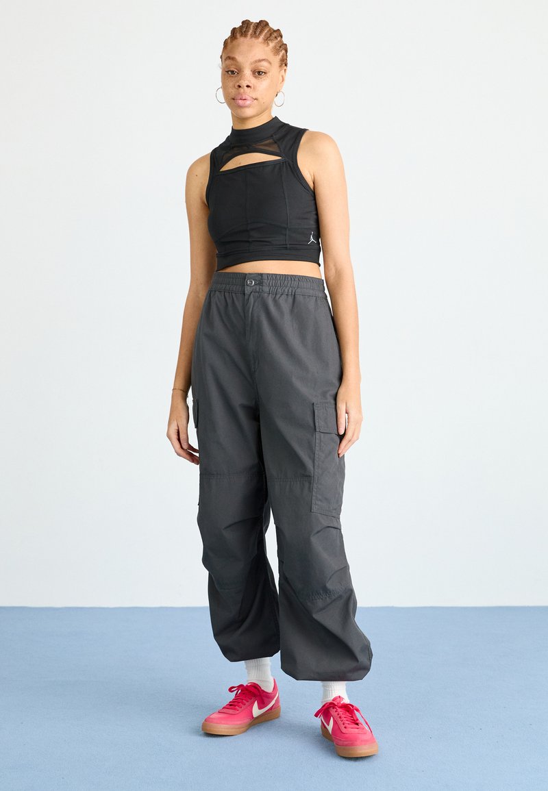Top corto negro con detalle recortado, combinado con pantalones cargo grises holgados. La modelo lleva zapatillas rosas y calcetines blancos.
