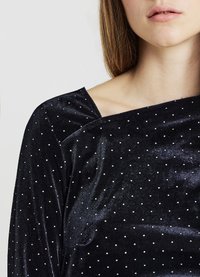 Schwarzes Samtoberteil mit leicht schulterfreiem Design, versehen mit silbernen Pünktchen. Glatte Textur, die weich am Körper fällt.