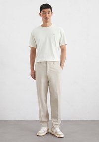 Cremefarbener Baumwoll-T-Shirt, beigen, gerade geschnittenen Hosen und weißen Sneakers mit beigen Akzenten. Lässiges Outfit mit einfachem Design und neutralen Farben.