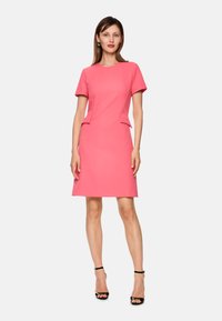 Rosa tailliertes Kleid mit kurzen Ärmeln, Peplum-Detail an der Taille und glatter Textur, kombiniert mit schwarzen, strappy High Heels.