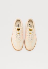 Baskets beiges avec des rayures rose clair, dotées d'une semelle en caoutchouc texturée, d'un design à lacets et d'un logo doré sur la languette.