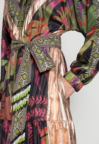 Abito a fantasia floreale nero, con tessuto bronzeo lucido, cintura decorata con perline geometriche e polsini elastici.