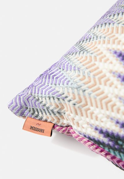 Dekoratívny vankúš s fialovým, béžovým a sivým zigzag vzorom a malou hnedou nálepkou s nápisom "MISSONI" na bielom pozadí.