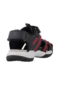 Sandalo sportivo nero e rosso con design aperto, cinturino in Velcro, interni imbottiti e suola in gomma. Presenta strisce a contrasto sulla parte superiore.