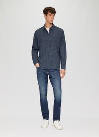 Donkerblauw geruite blouse met lange mouwen, gecombineerd met slim-fit blauwe jeans en witte sneakers; een schone, casual uitstraling.