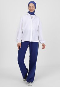 Hvid skjorte med ballonsleeves parret med løse marineblå bukser. Modellen bærer en blå hijab og sorte sneakers.