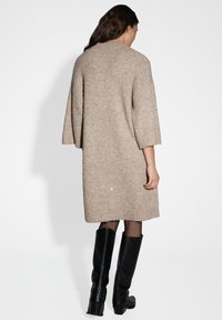 Abito lavorato a maglia color carne con una vestibilità comoda, maniche oversize e texture a coste, abbinato a stivali alti neri in pelle.