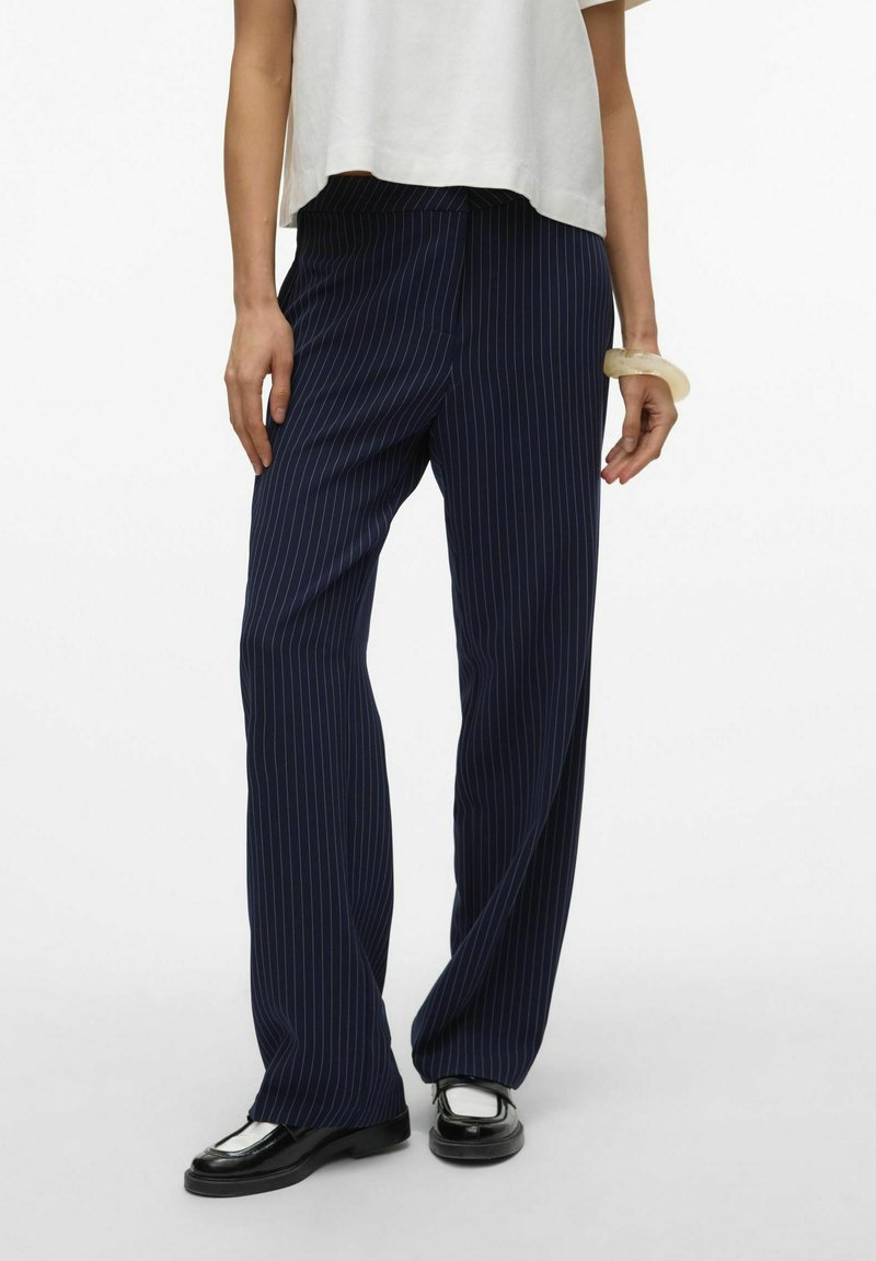 Navyblå randiga byxor med lös passform, tillverkade av lättviktsmaterial. Har en rak midja och sidfickor, i kombination med svarta skor.